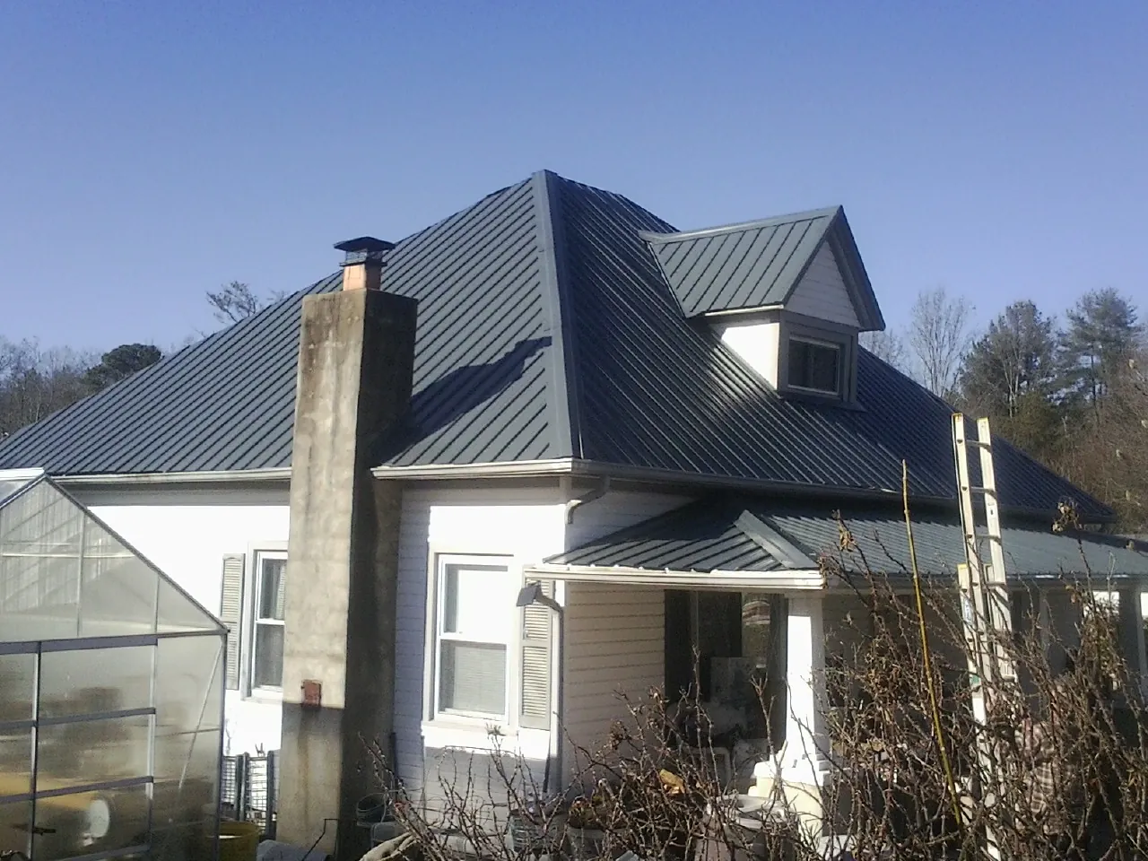 Dark blue standing seam metal roof on a white farmhouse with dormer — Slate & Tile Roof Repair by Roofing Brothers in Sloan