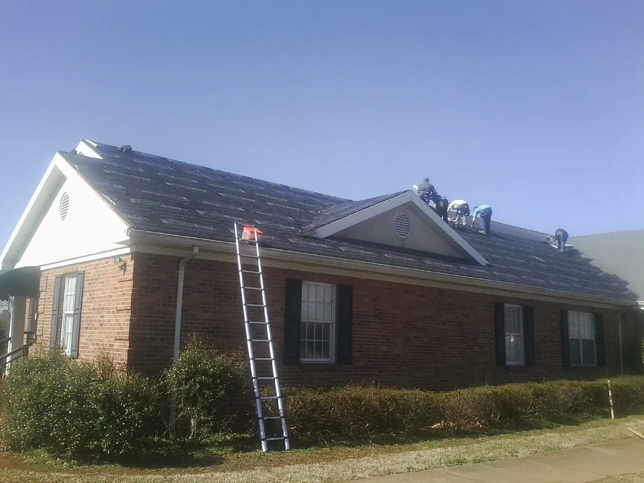 Crew tearing shingles off a brick ranch roof with a ladder set — Metal Roof Repair work by our crew in Sloan