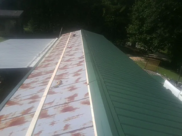 Old rusted panels beside newly installed green metal roofing — Wind Damage Roof Repair by Roofing Brothers in Sloan