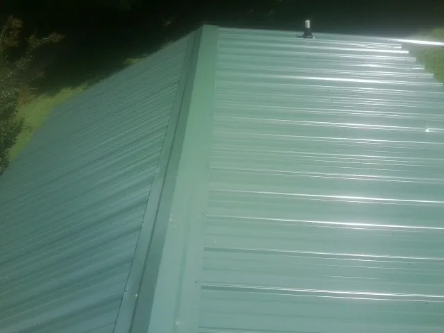 New green metal panels meeting at the ridge of a roof — Flat Roof Repair work by our crew in Sloan