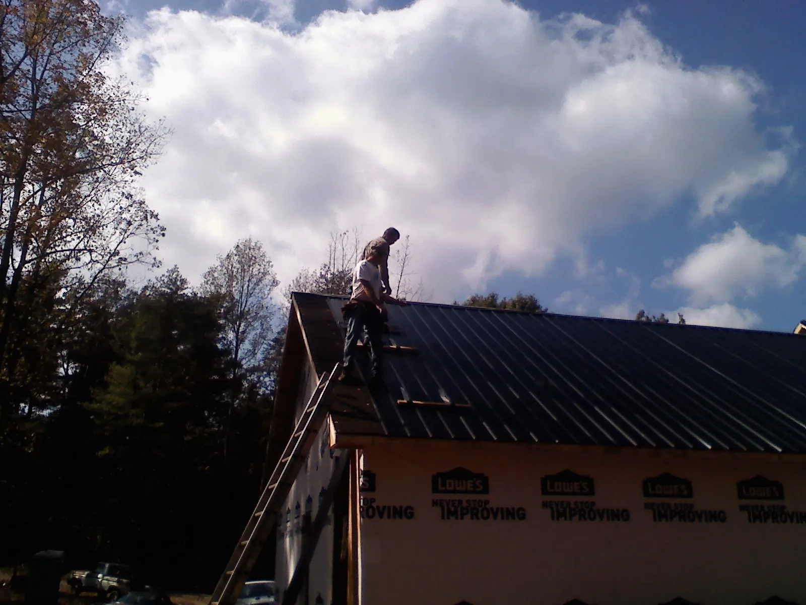 Roofer fastening dark metal panels high against a cloudy sky, from a Roof Inspection job in Sloan