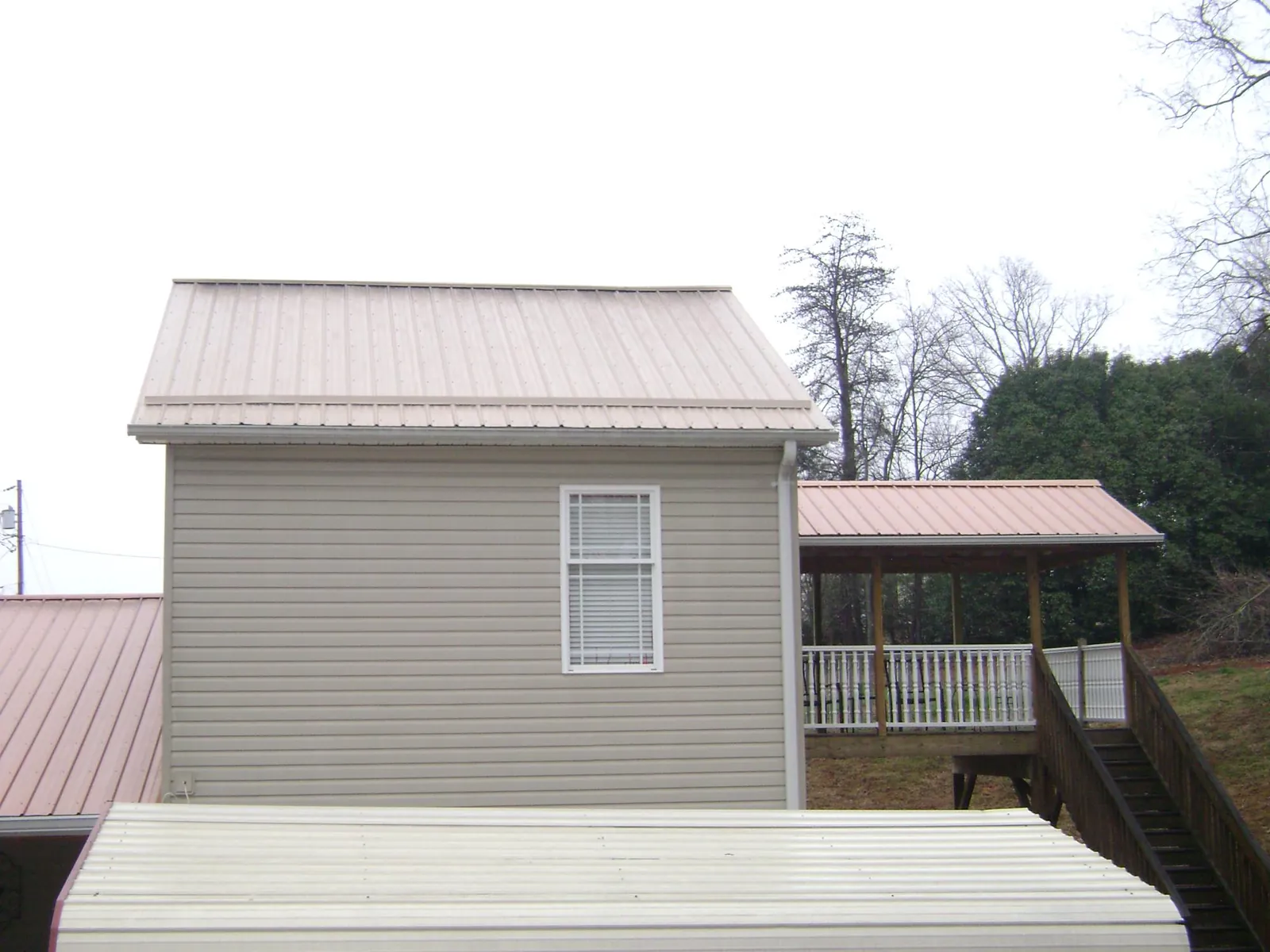 Tan metal roofs on a two story addition and attached porch, from a Roof Replacement job in Sloan